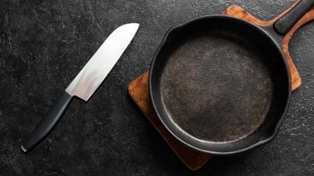 Knife, cast iron pan and cutting board on black background.