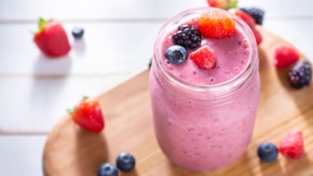 A finished smoothie—made with strawberries, blueberries, raspberries, and blackberries—sits atop a cutting board.