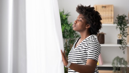 person standing in front of window holding curtain while breathing deeply