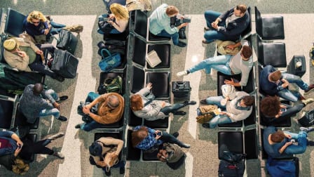 overhead view of rows of seats at airport gate with people waiting with luggage