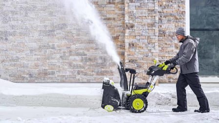 A man pushing a Ryobi RY40870 Snow Blower through snow on a driveway