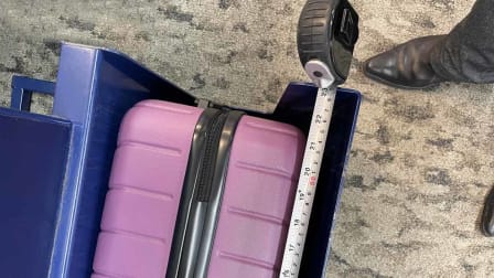 overhead view of measuring tape on metal bin designed to test size of carry-on luggage with pink luggage in bin