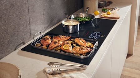 LG Studio CBIS3618BE in kitchen with white countertop and cabinets, with pan of chicken with capers and lemons, pot of mashed potatoes, and skillet with green beans
