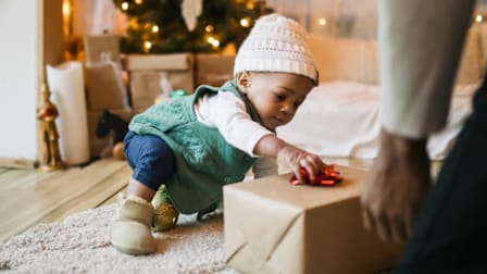 a baby reaching out for a gift wrapping bow on a present