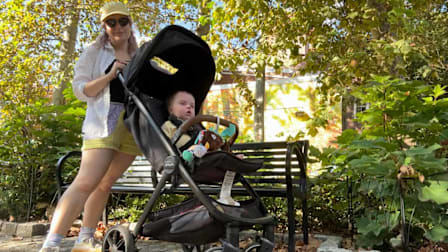 baby in Nuna TRVL LX stroller with parent pushing stroller, in park in front of a park bench