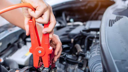 a person jump-starting a dead car battery with a jumper cable