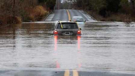 Cars submerged in floodwater on road.