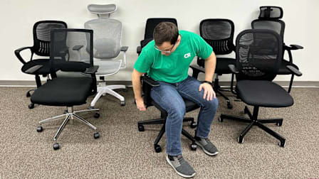 person wearing green Consumer Reports shirt, sitting in office chair with 7 other office chairs surrounding them