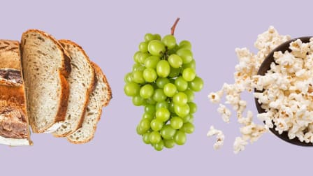 overhead view of sourdough bread with cut slices, bunch of green grapes, and bowl of popcorn with some popcorn spilled out