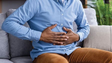 close of up person's torso with their hands over stomach as in pain, sitting on couch