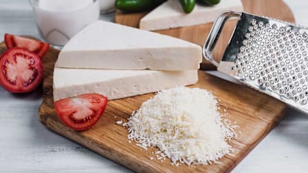 Grated cojita cheese on a cutting board with tomatoes and jalapenos