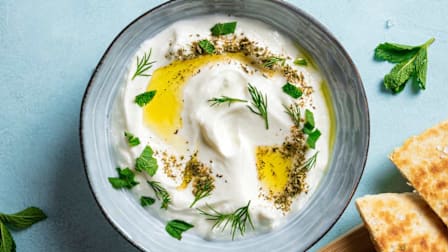 Labneh topped with herbs and olive oil in a bowl next to pita bread