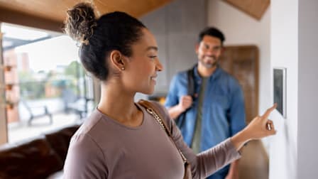 Couple leaving their house and setting the alarm using a home automated system.