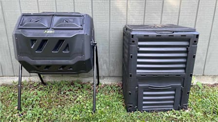 two different styles of black compost bins side-by-side in front of side of grey shed