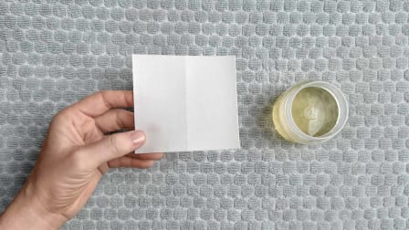 hand holding laundry detergent sheet next to liquid laundry detergent in cup