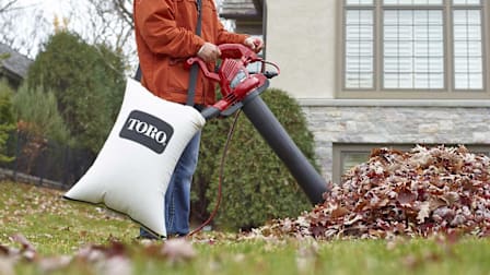 detail of person using Toro UltraPlus 51621 to vacuum leaves on lawn in front of house