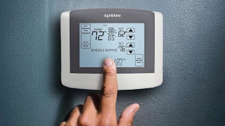 person's finger touching screen of Aprilaire 8600 programmable thermostat
