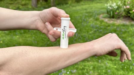 detail of person's hands and arms using Bug Bite Thing on forearm with grass in background