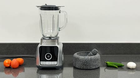 a blender, a Molcajete and ingredients for salsa on a kitchen counter top