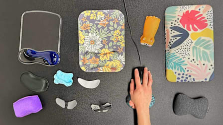 overhead view of 12 different styles and types of wrist rests with hand holding mouse using one of the wrist rests