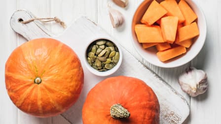Pumpkin, pumpkin seeds, and sliced pumpkin on white wood cutting board.
