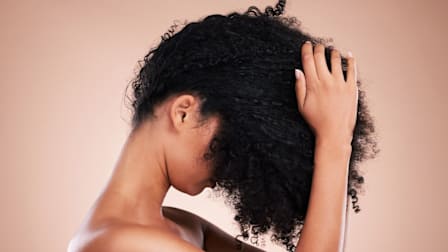 person with black curly hair pulled over in front of their face, hands in their hair
