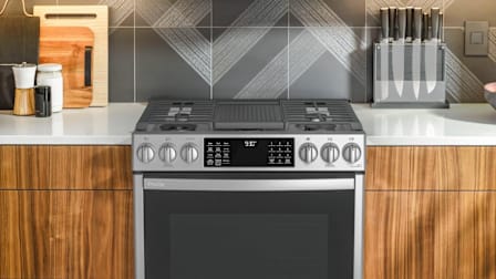 GE Profile CGI50042101 range in kitchen with wooden cabinets, white countertop, and grey backsplash with cutting boards and knives on countertop