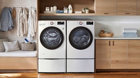 LG WM4000HWA washing machine and LG DLHC4002W dryer in laundry room with wood floor and cabinets, clothes hanging to the left of machines