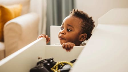 A young child peeks over the edge of an open drawer, holding onto the sides