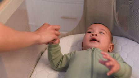 adult holding baby's hand, baby is in Maxi-Cosi Iora Bedside Bassinet
