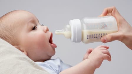 Baby holding their mouth open for a waiting bottle filled with milk.
