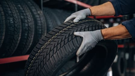 close up of person wearing gloves while holding tire, rack of tires in the background