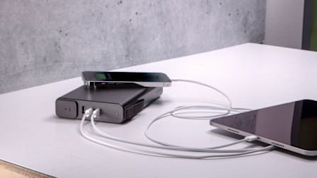 Mophie Powerstation Pro AC 27,000mAh 100W portable charger charging a phone and tablet on a table.