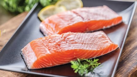 two raw salmon filets on square black plate with parsley and lemon slices as garnish