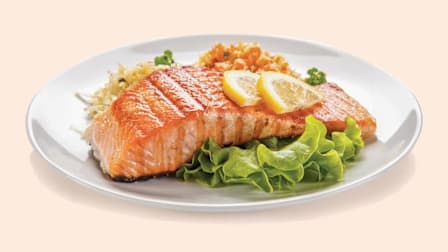 A plate with cooked grains, vegetables and salmon, garnished with lemon slices.