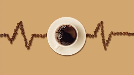 A cup of black coffee in a white saucer, viewed from above, with coffee beans arranged on both sides to form the shape of a heartbeat line on a light brown background.