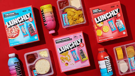 Multiple 'Lunchly' branded lunch kits 'The Pizza', 'Fiesta Nachos', and 'Turkey Stick ‘Ems'.and PRIME hydration drinks on a red background.