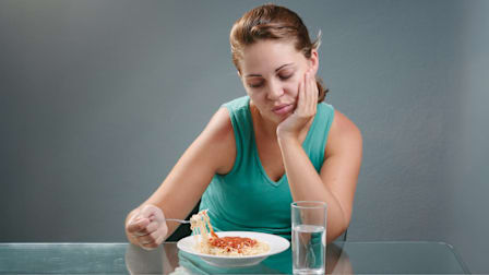person sitting at table contemplating whether or not they want to eat a bowl of pasta with tomato sauce