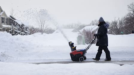 Woman pushing a snow blower in a driveway