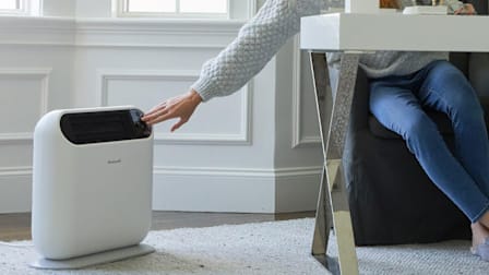 detail of person sitting at desk, reaching to adjust setting on Honeywell Thermawave 6 HCE870W space heater