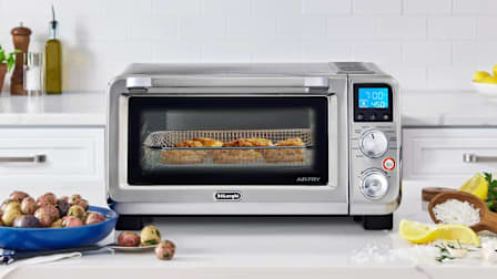 Coconut Shrimp being baked in a DeLonghi EO141164M on a kitchen counter next to ingredients and prepared foods.