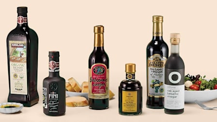 Six bottles of balsamic vinegar displayed with bread and bowl of salad