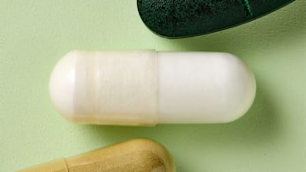 Three supplement pills on a light green surface