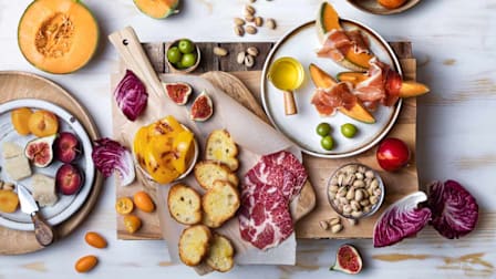 a charcuterie board with fruits, vegetables, olives, meats, bread, cheese and nuts.