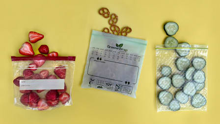An Amazon Basics bag holding strawberries, a GreeneWrap bag with pretzels, and a Glad Flex’N Seal bag containing cucumber slices on a yellow background.