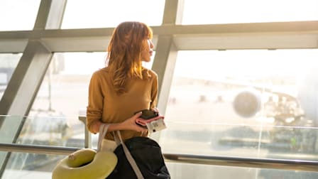 A woman holding a carry on bag and a travel pillow at an airport.