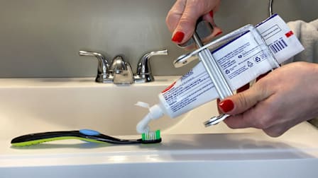 Hands holding toothpaste tube with crank squeezer attached on bathroom sink