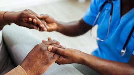 Healthcare works examining the fingernails of a Black patient.