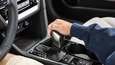 A hand holding the gear shift of an automatic car.