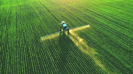 high angle view of tractor spraying fertilizer on green field